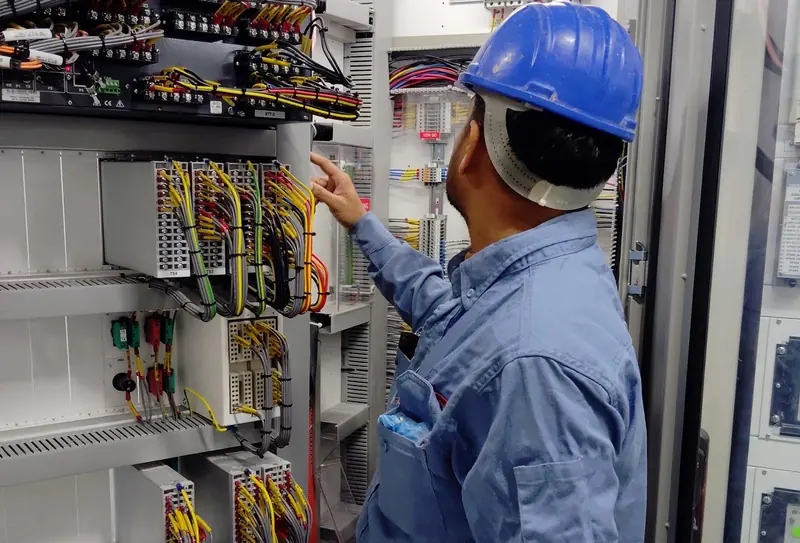 Technician in a hard hat checking wiring in a control panel